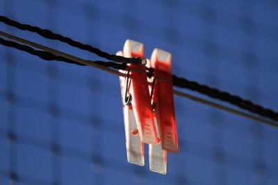 Close-up of red clothespins hanging by fence against sky