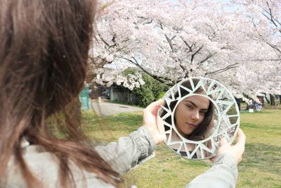 Reflection of teenage girl on mirror against cherry blossoms