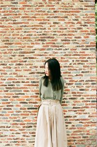 Portrait of a young woman standing against brick wall