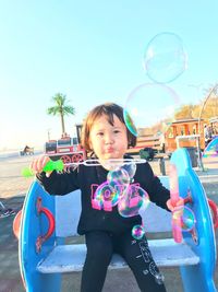 Portrait of girl with bubbles in park against sky
