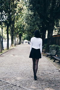 Rear view of woman walking on footpath amidst trees