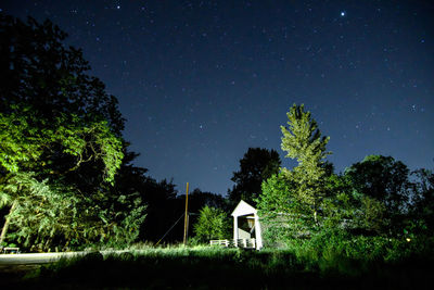 Covered bridge by trees against star field at night