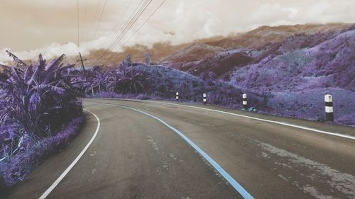 Empty road amidst plants and mountains against sky