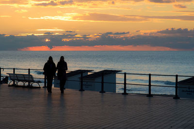 Rear view of silhouette people overlooking calm sea at sunset