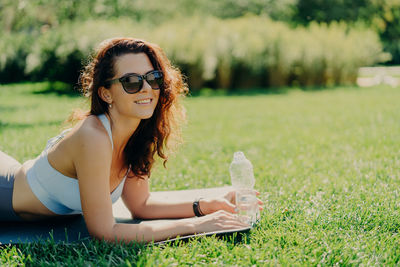 Portrait of smiling woman wearing sunglasses lying on mat in park