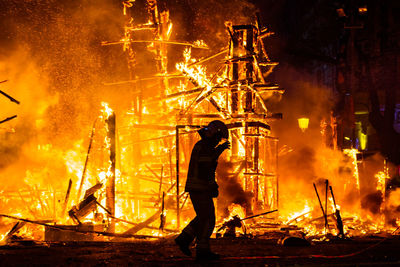 Full length of firefighter standing against fire