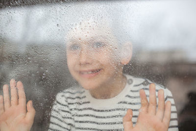 Smiling boy looking through wet window