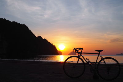 Silhouette bicycle on beach against sky during sunset