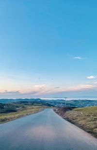 Empty road amidst land against blue sky