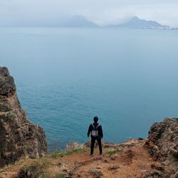 Rear view of man standing on rock by sea