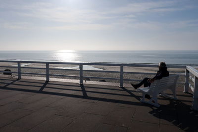 Man sitting on bench by sea against sky during sunny day
