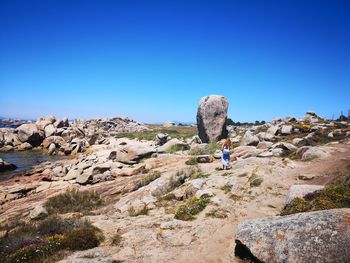 Rear view of people on rock against clear blue sky