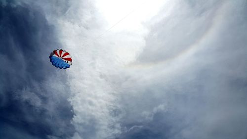 Low angle view of people parasailing against cloudy sky