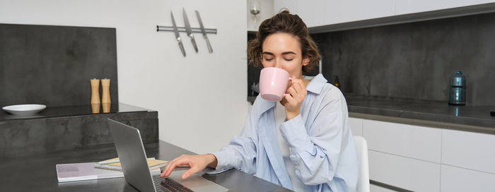 Young woman drinking coffee while standing against wall