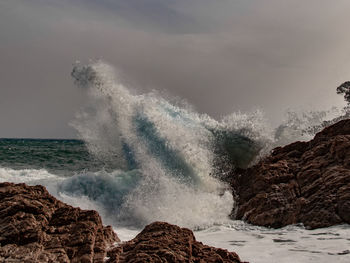 Waves splashing on rocks at shore against sky