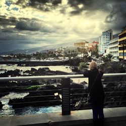 Woman standing by railing against cloudy sky