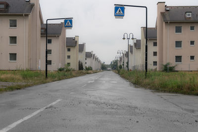 Empty road amidst buildings against sky in city