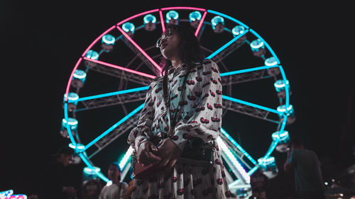 Low angle view of woman standing against ferris wheel at night