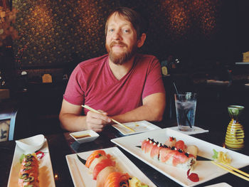 Portrait of smiling man sitting by food on table at restaurant