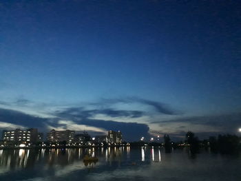 Illuminated buildings by river against sky at night