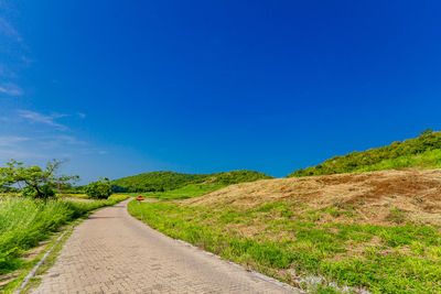 Empty road amidst field against blue sky