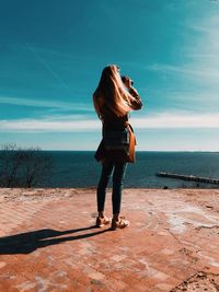 Full length rear view of woman standing by sea against sky during sunny day