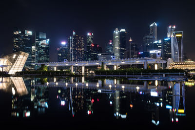 Illuminated buildings by river against sky at night