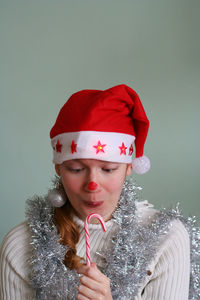 Close-up smiling woman in santa hat holding candy against wall