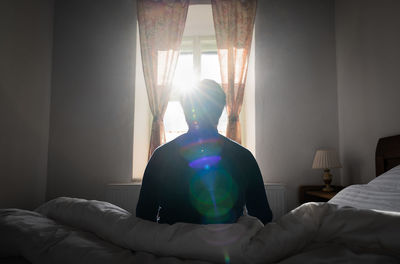 Rear view of man relaxing on bed at home