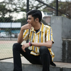 Young man looking away while sitting on bench