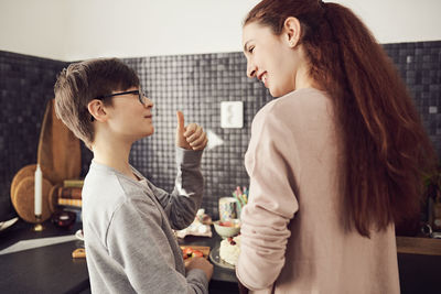 Boy gesturing thumbs up to sister while preparing food at kitchen