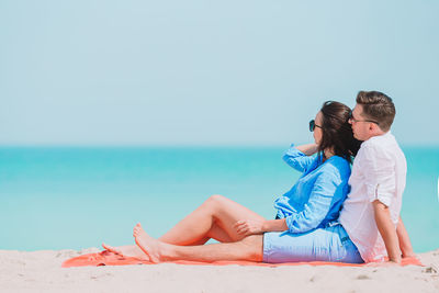 Rear view of woman sitting on beach against sky