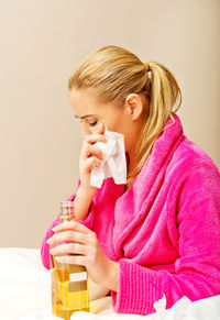 Woman holding bottle while wiping teardrops with facial tissue at home