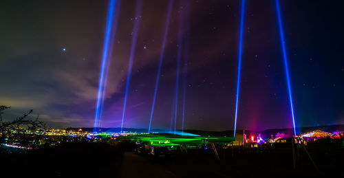 Panoramic view of illuminated lights against sky at night
