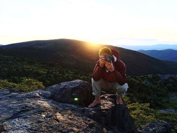 Full length of young woman standing on rock against sky during sunset