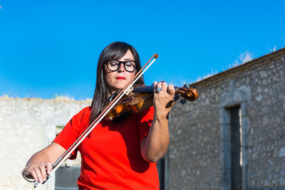 Woman playing violin while standing against built structure