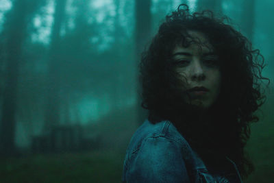 Portrait of young woman standing in forest during foggy weather