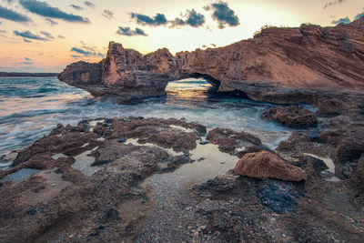 Rocks on beach against sky during sunset