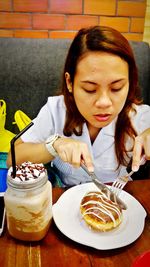 High angle view of young woman having donut with milkshake at table in restaurant