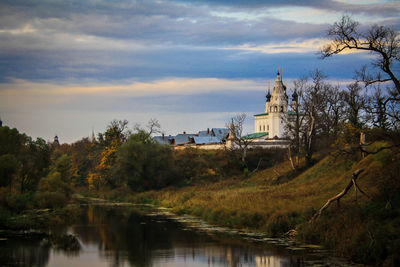 Church by river against cloudy sky