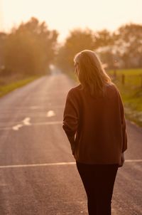 Rear view of woman standing on road during sunset