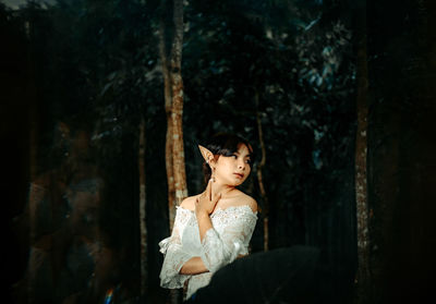 Woman looking away while standing against tree trunk