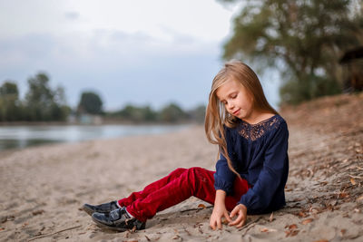 Full length of girl sitting on sand at lakeshore