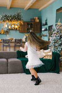 A girl with long hair in a white dress is spinning in the living room, with a christmas tree