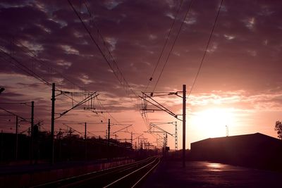 Power lines on road against sky during sunset