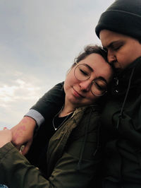 Romantic woman kissing on girlfriend forehead against sky