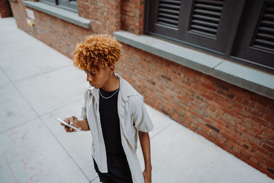 Portrait view of the multiracial man typing sms while standing near the brick wall