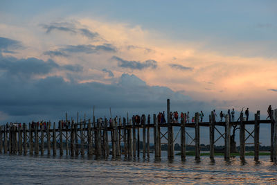 People on footbridge over sea against sky during sunset