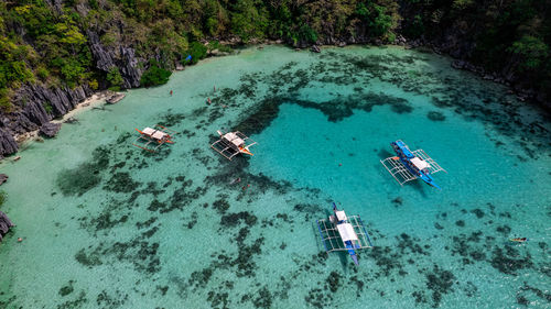 In the photo, a vibrant tropical boat near a beautiful beach or rocky shore.