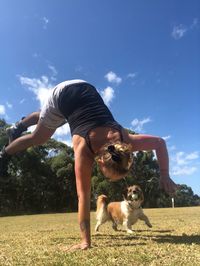 Young woman playing with dog on field against sky